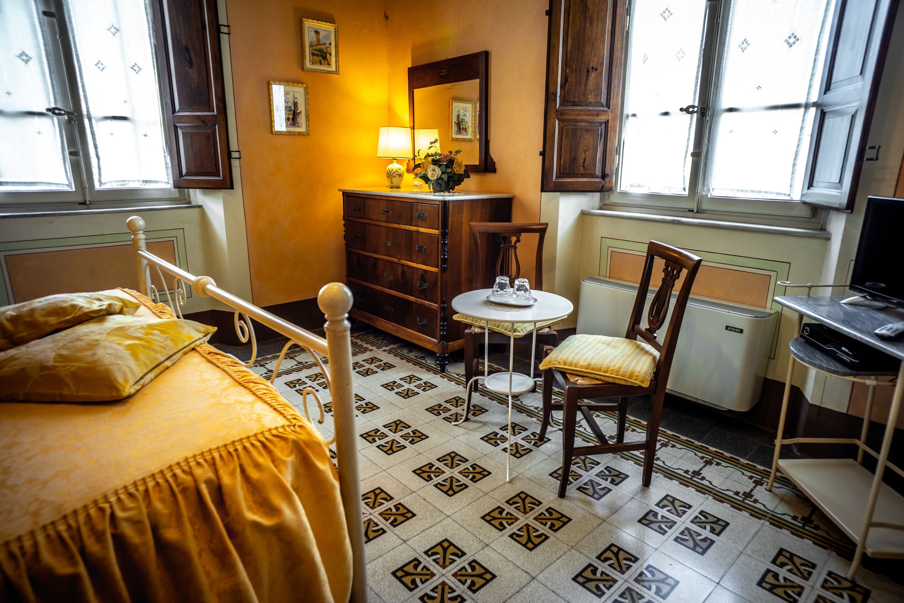 Une chambre à coucher comprenant un lit, une chaise, une commode, une petite table avec une lampe et un téléviseur.