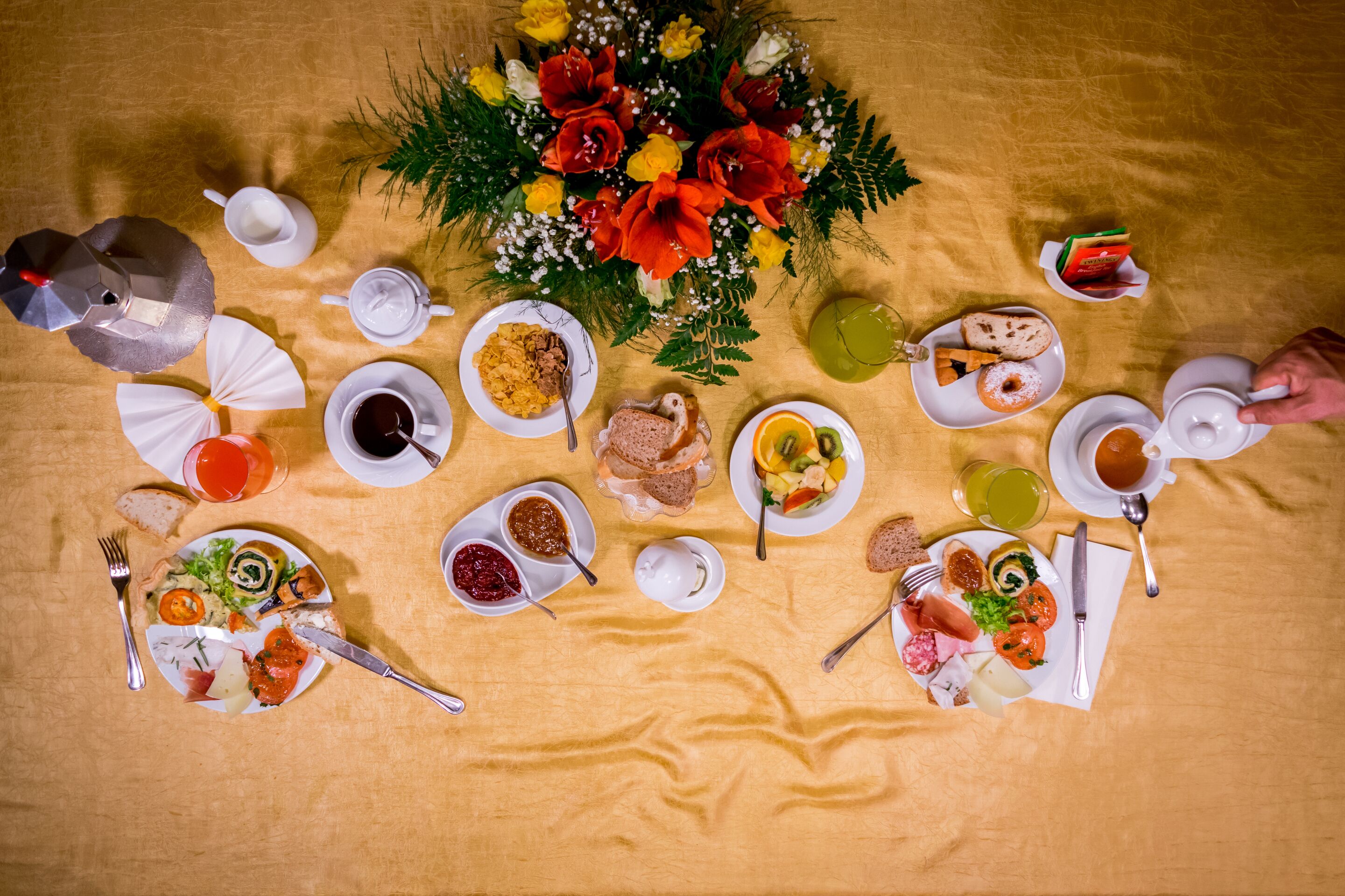 Ein Tisch ist reichhaltig mit Speisen gedeckt, darunter Brot, Obst und eine Blumenarragemement.