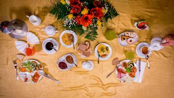 Ein Tisch ist reichhaltig mit Speisen gedeckt, darunter Brot, Obst und eine Blumenarragemement.