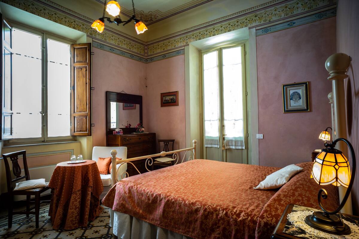 A bedroom with a bed, a chair, a table, a lamp, and a dresser.