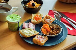 A breakfast setting with a cup of coffee, a bowl of fruit, and a plate with toast and nuts.