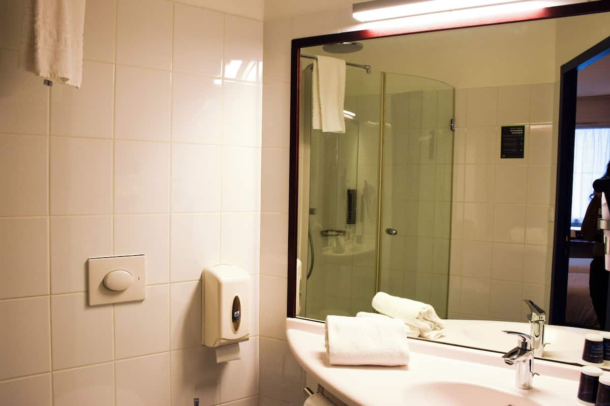Une salle de bain avec un lavabo blanc, un miroir, un porte-serviettes et une douche à parois de verre.