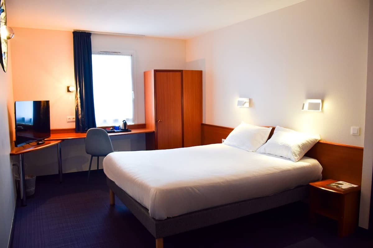 Une chambre d’hôtel comprenant un lit, un bureau avec une chaise, une télévision et une armoire.