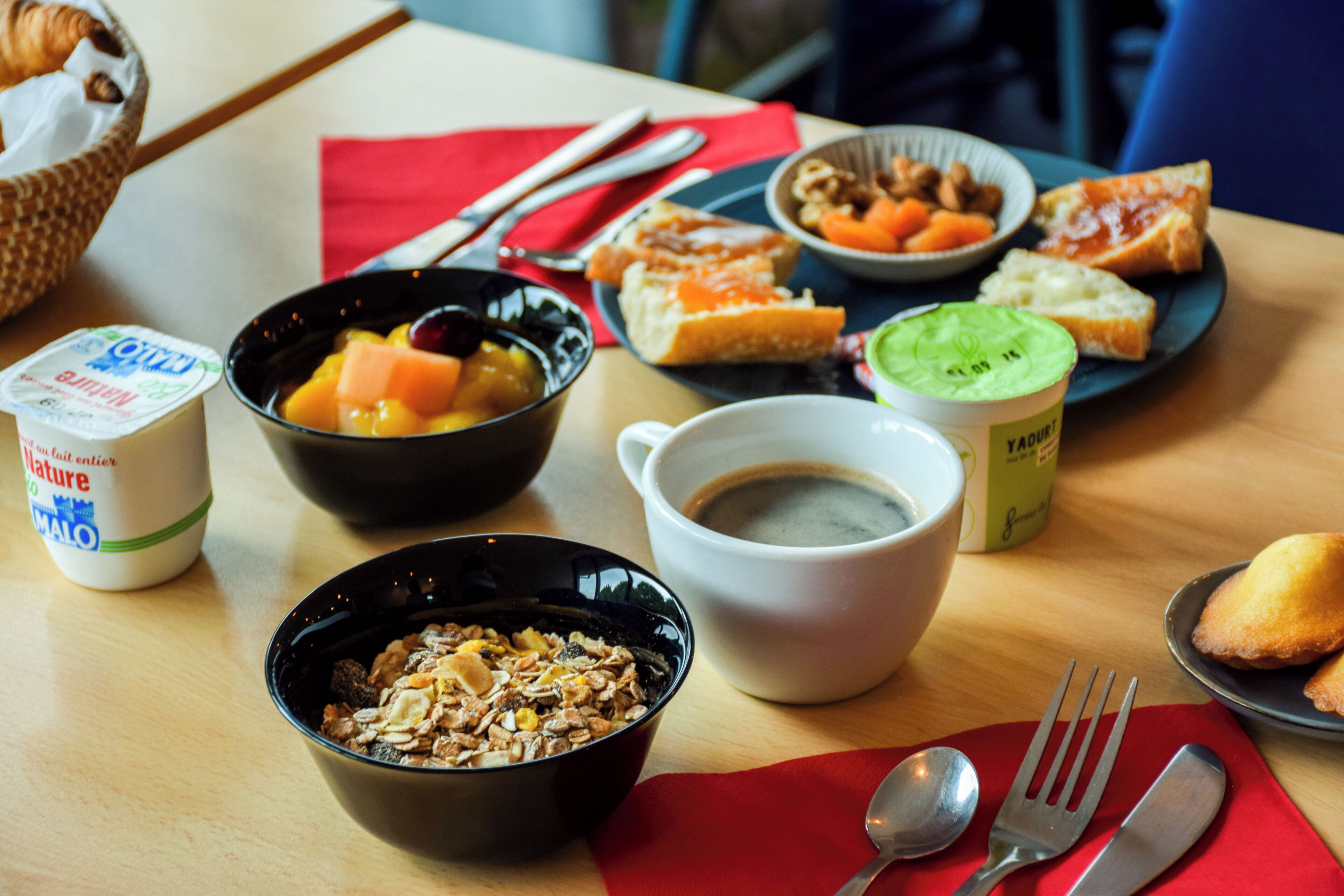Una mesa de desayuno con diversos alimentos, como cereal, yogur, fruta y tostadas.