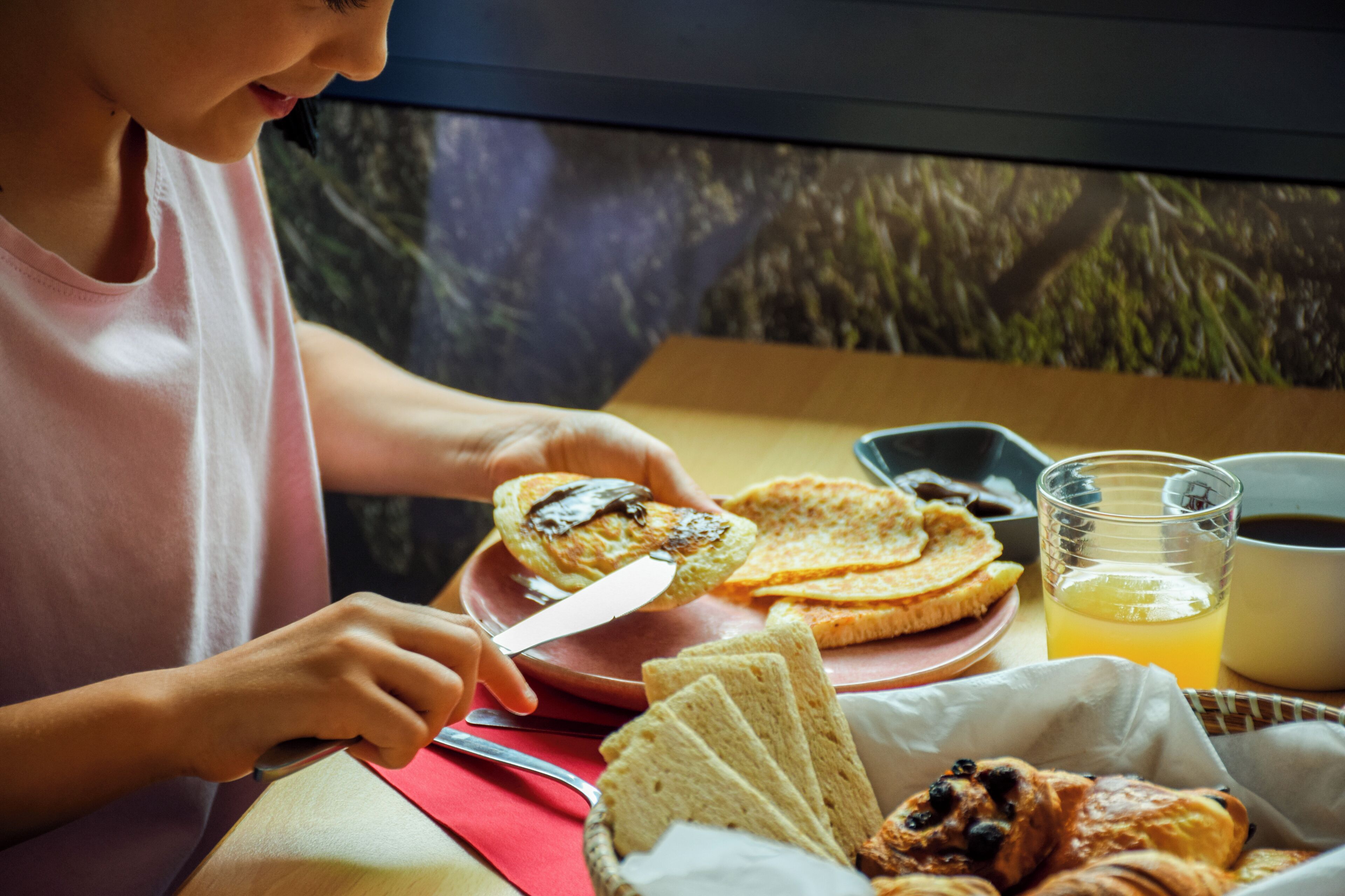 Una persona sentada a una mesa con un desayuno que incluye tostadas, un croissant y un vaso de jugo de naranja.