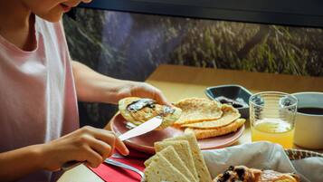 Una persona sentada a una mesa con un desayuno que incluye tostadas, un croissant y un vaso de jugo de naranja.