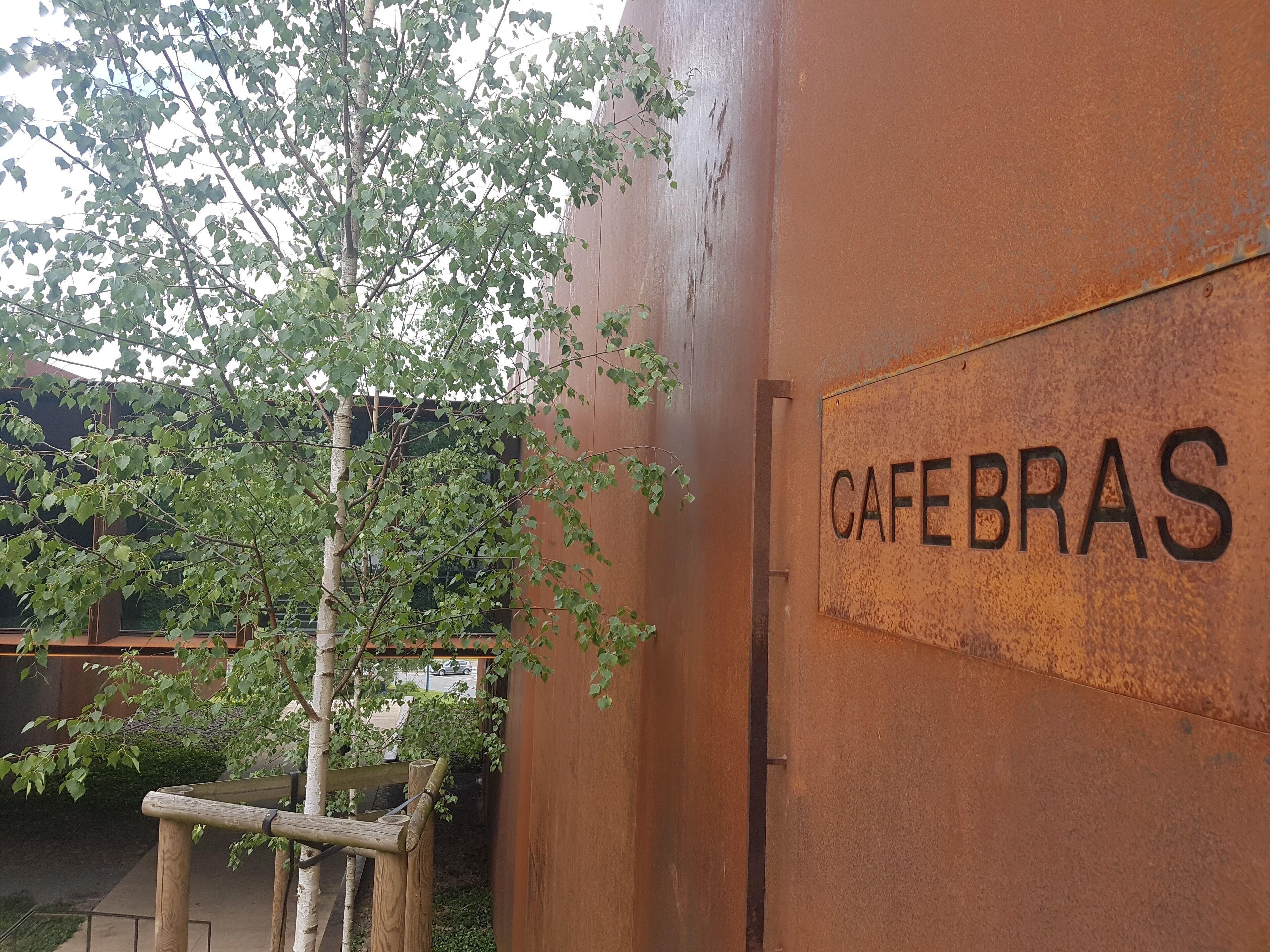 Un mur en métal rustique sur lequel est inscrit le mot « CAFEBRAS » et un banc en bois.