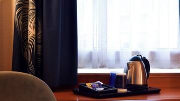 Quarto de hotel com janela, cortinas, bandeja com chaleira, xícara e caixa de lenços.