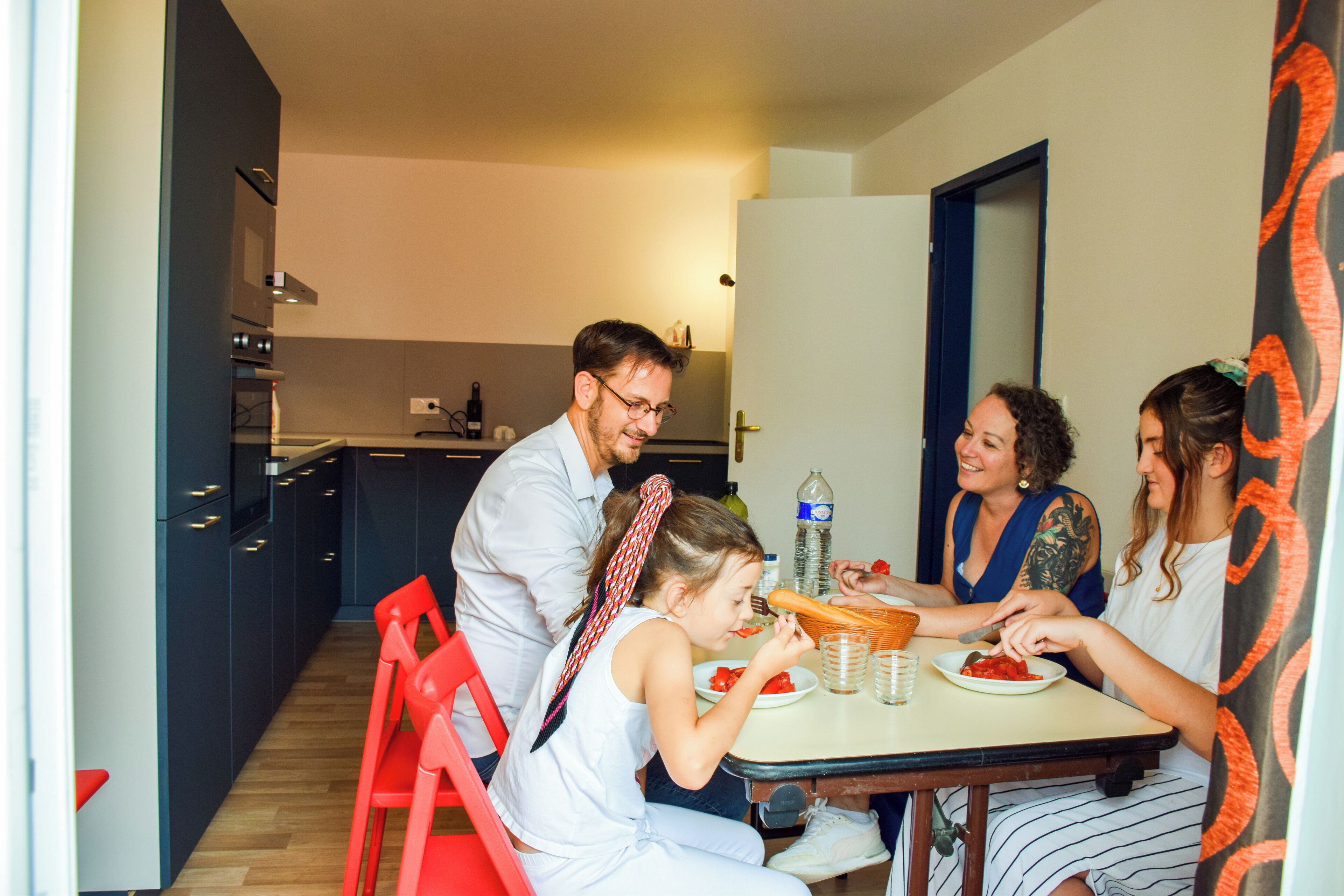 A modern kitchen with dark cabinets, a dining table, and red chairs.