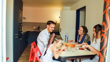 A modern kitchen with dark cabinets, a dining table, and red chairs.
