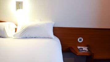 A hotel room with a neatly made bed, a bedside table with a lamp, and a wall-mounted control panel.