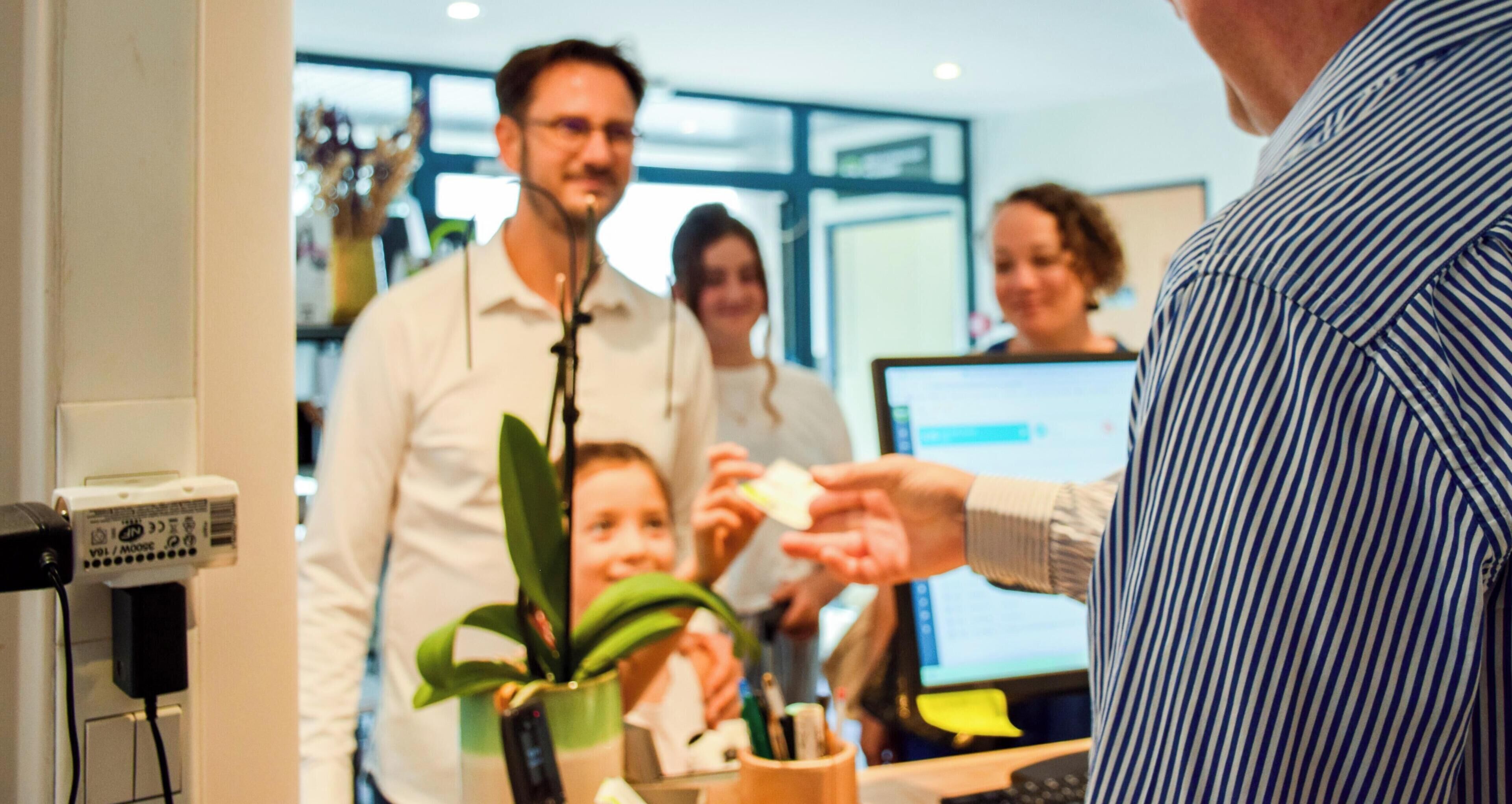 A person handing a card to another person in a modern indoor setting with a computer monitor and a plant.