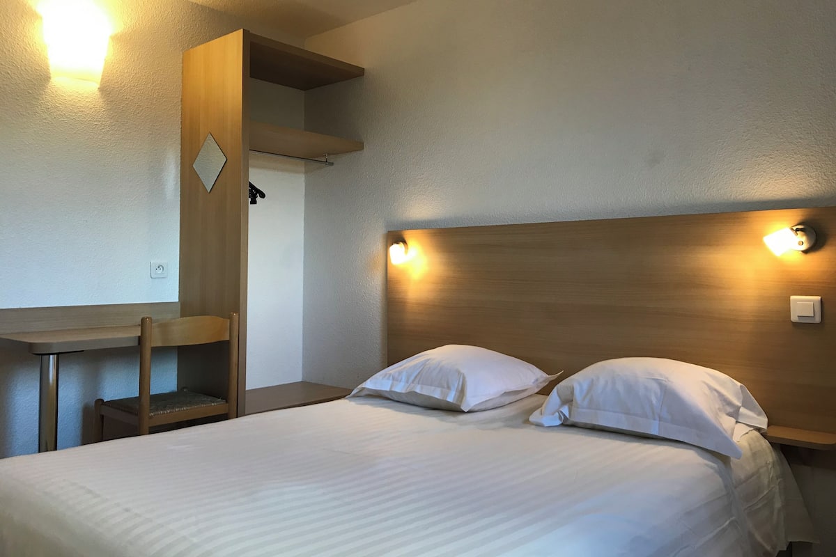 A hotel room with a bed, two bedside tables, a desk, and a chair.