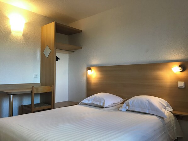 Una habitación de hotel con una cama, dos mesitas de noche, un escritorio y una silla.