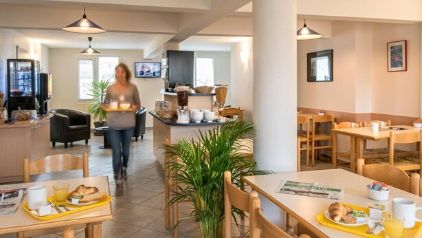 Uma área de refeições moderna em hotel, com mesas e cadeiras de madeira e um ponto central de serviço.