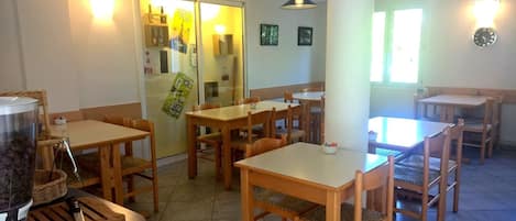 Comedor con mesas y sillas de madera, una máquina de café y un refrigerador.