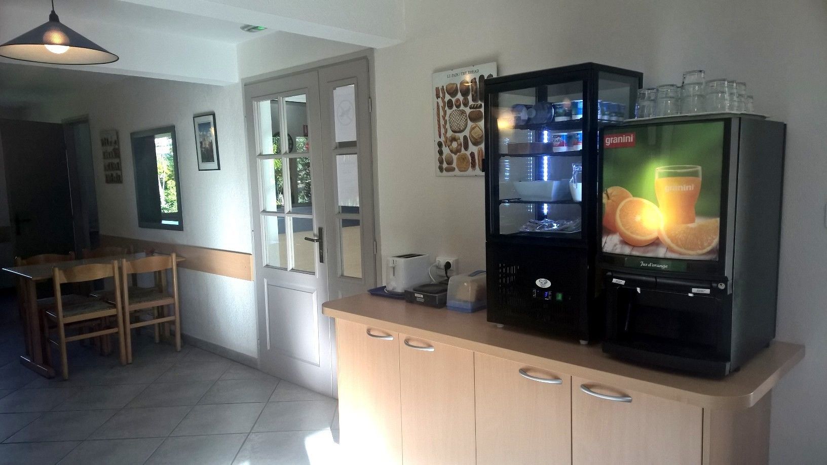 A kitchen with a refrigerator, a coffee machine, and a dining table with chairs.