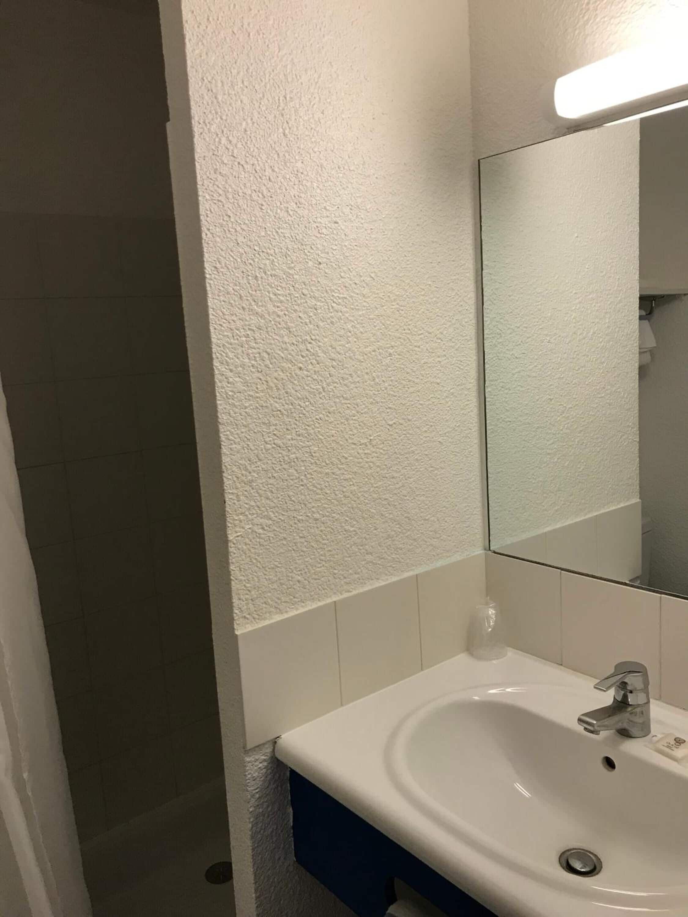 A bathroom with a white sink, a mirror, and a shower area.