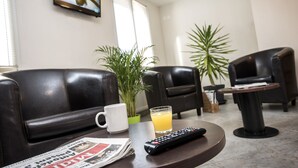 Uma sala de estar com poltronas de couro, uma mesa de centro, um controle remoto, um copo de suco de laranja, um jornal e um vaso de planta.