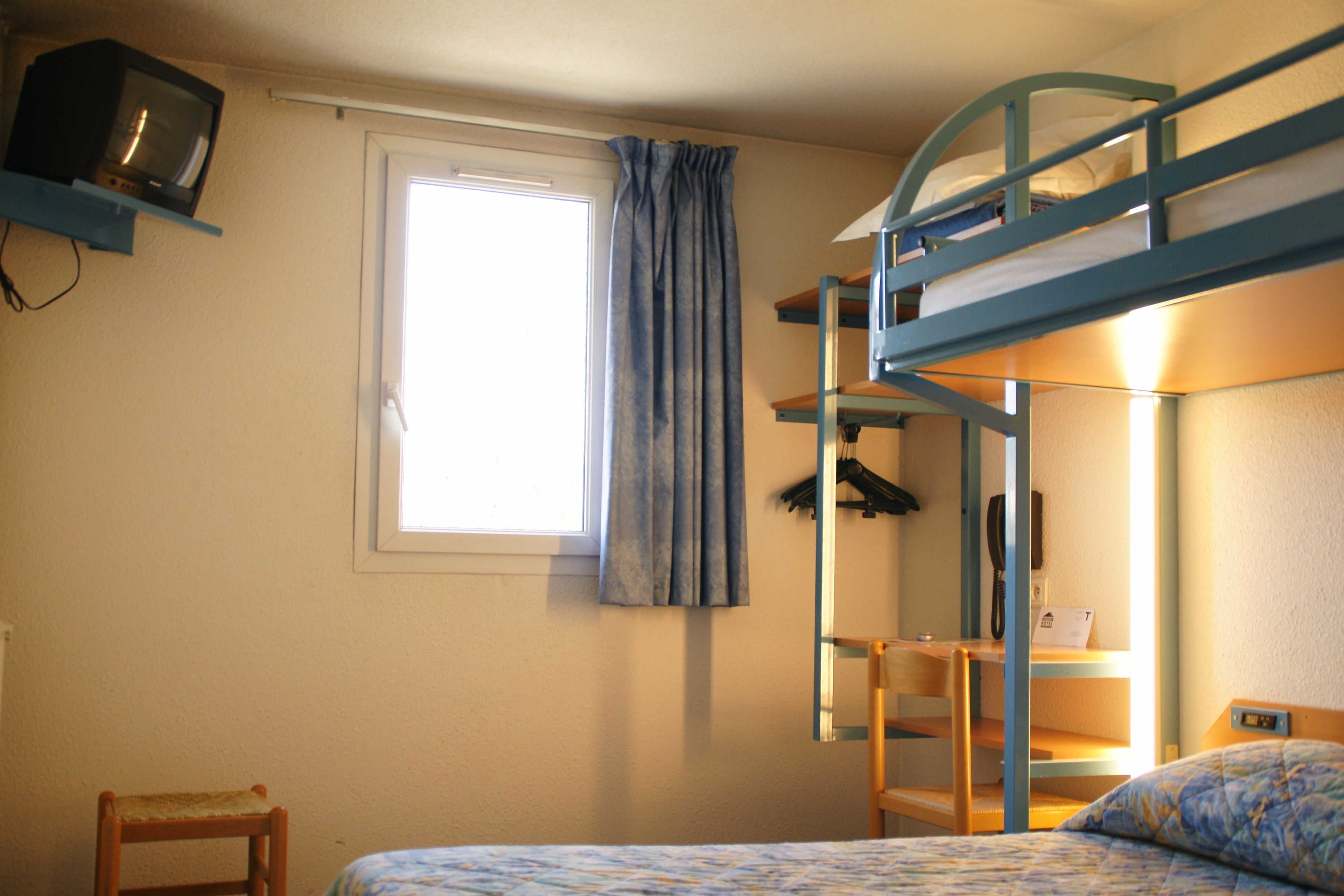 Habitación con literas, un televisor en un estante, una ventana con cortinas y una silla.