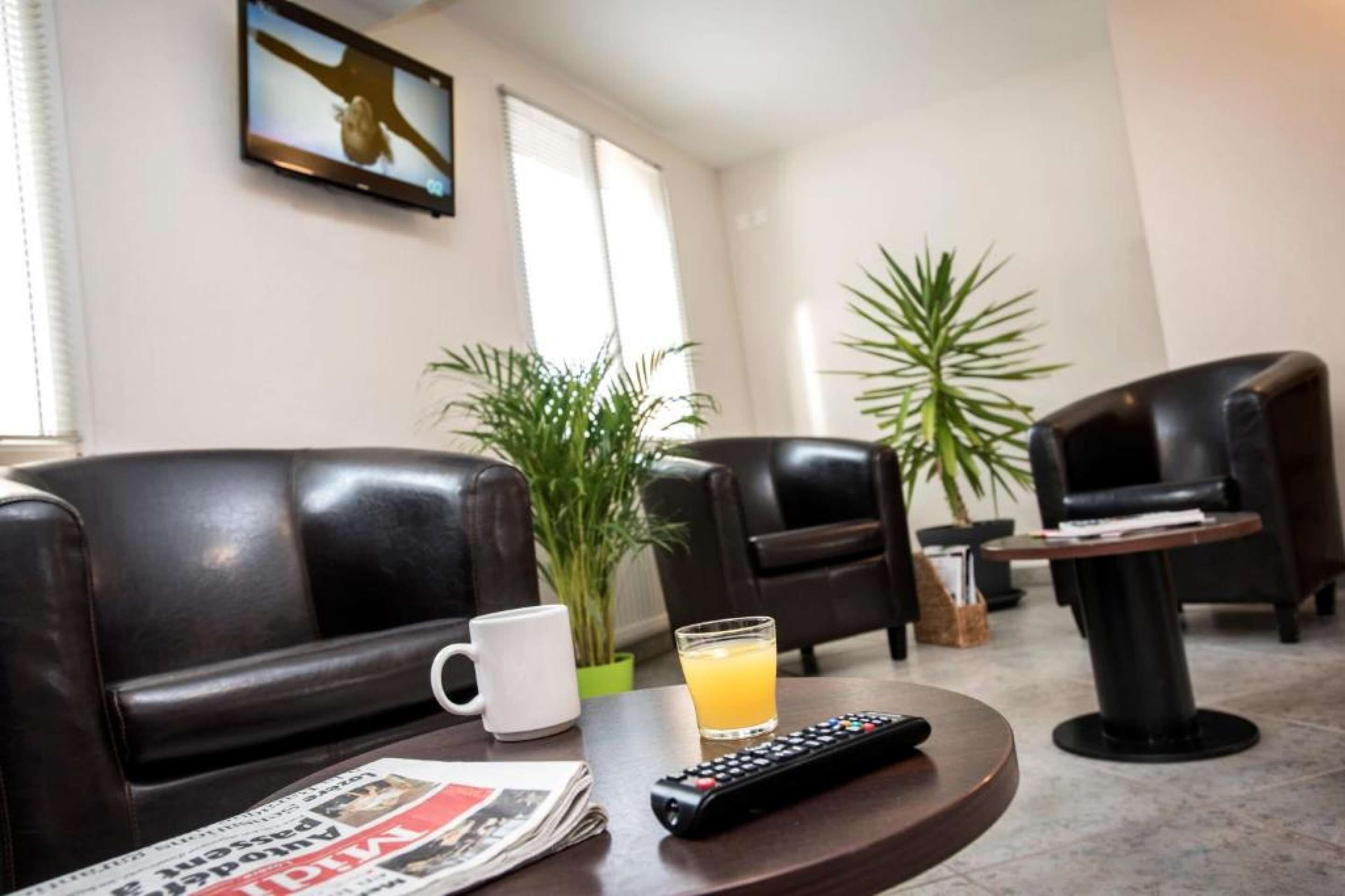 Een hotelkamer met lederen fauteuils, een bijzettafeltje, een krant, een glas sinaasappelsap, een afstandsbediening en twee potplanten.