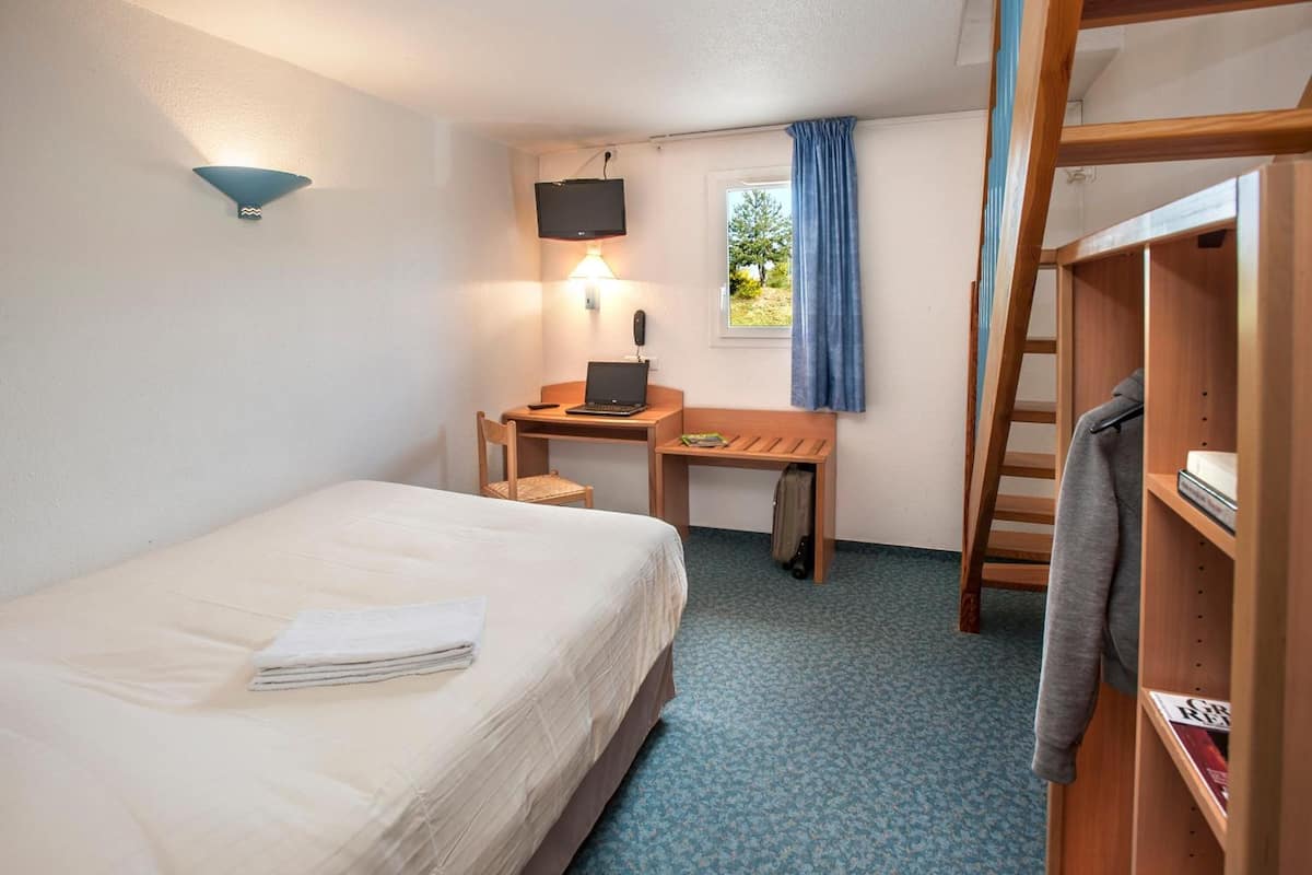 Ein Hotelzimmer mit Bett, Schreibtisch, Laptop und Fernseher.
