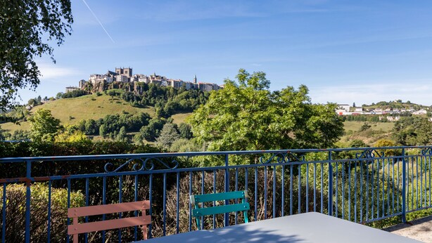 A terrace with a table and benches overlooking a hill with a castle-like structure. - Brit Hotel Essentiel St Flour (Saint-Flour)