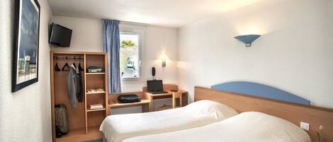 A hotel room with two beds, a desk with a laptop, a TV on the wall, and a closet with hanging clothes.