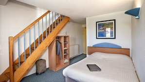 A bedroom with a wooden staircase, a bed, a bedside table, a framed picture on the wall, and a coat rack with clothes. - Brit Hotel Essentiel St Flour (Saint-Flour)