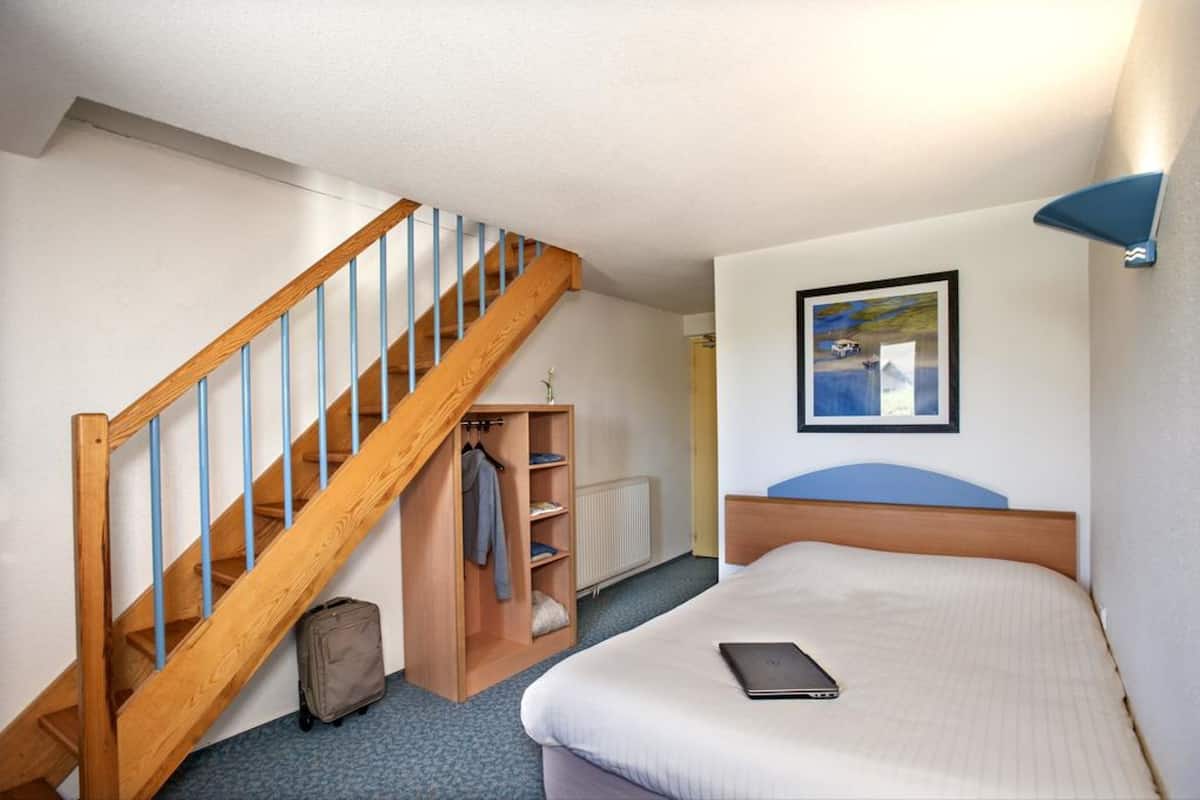 Ein Schlafzimmer mit einer Holztreppe, einem Bett, einem Nachttisch, einem gerahmten Bild an der Wand und einem Kleiderständer mit Kleidung.