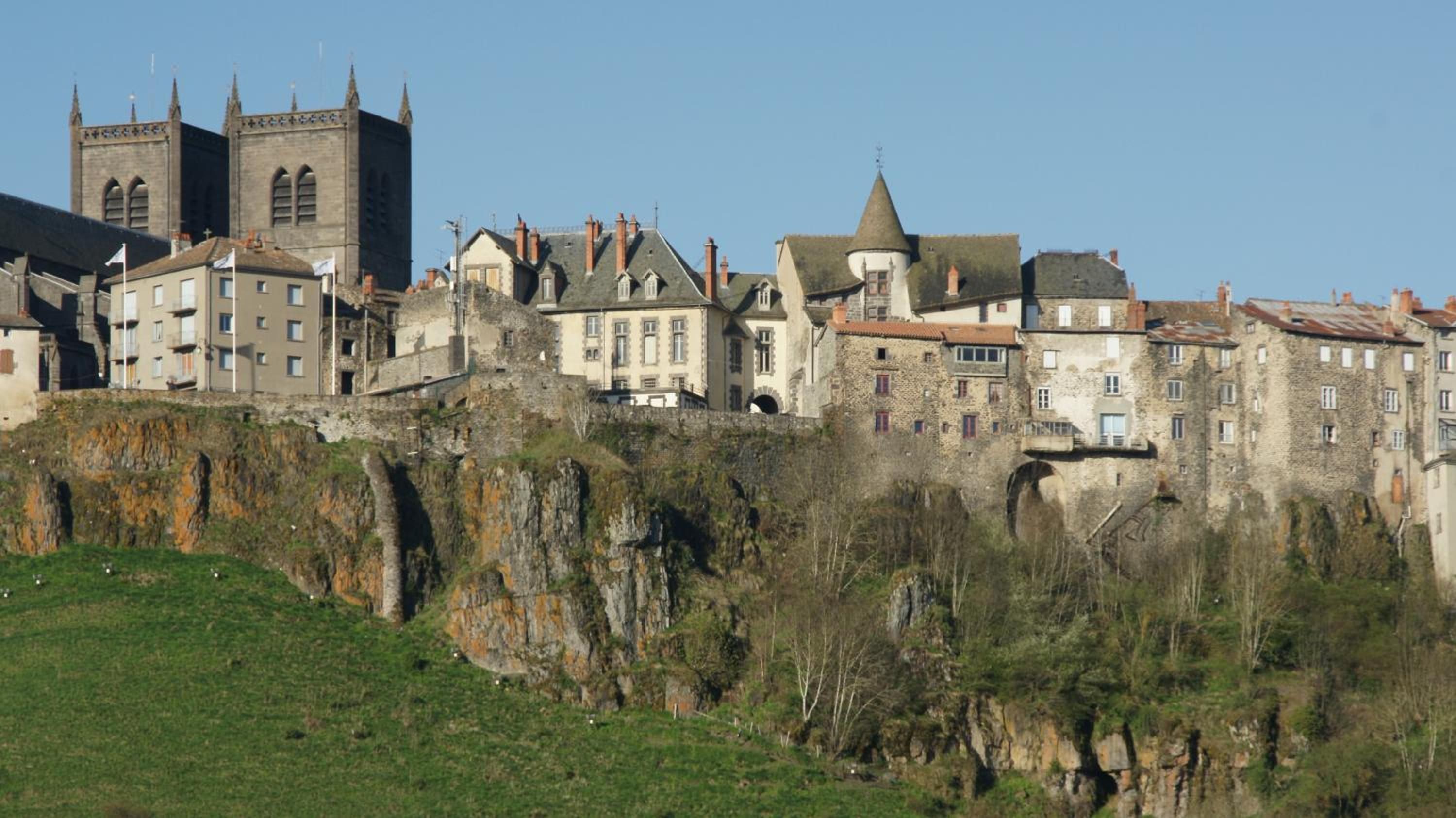 A historic town with stone buildings, a prominent church tower, and a steep cliff.