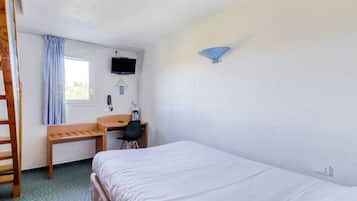 Ein kleiner, sauberer Raum mit einem Bett, einem Schreibtisch, einem Stuhl, einem Fernseher und einem Fenster mit Vorhängen.