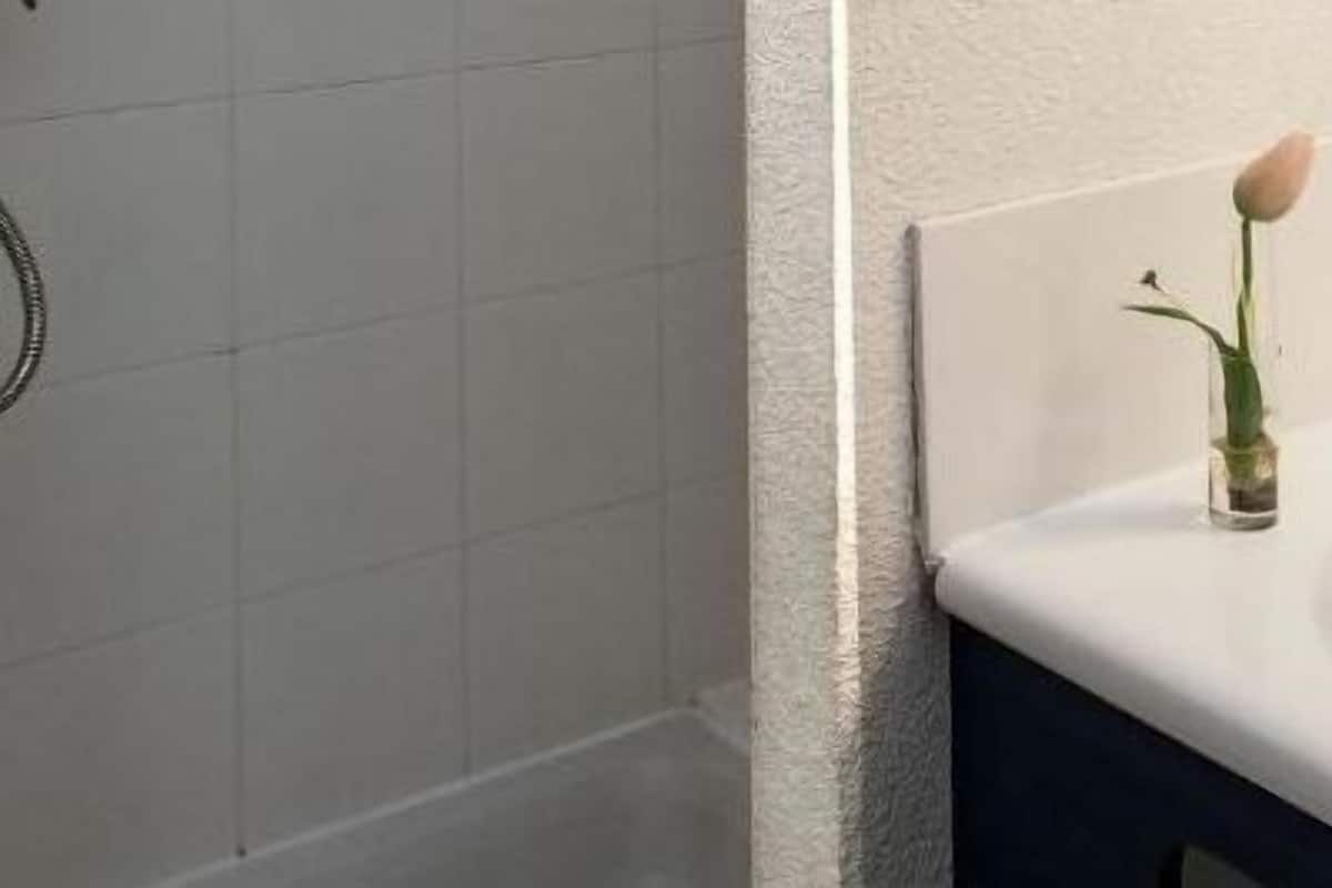 Ein Badezimmer mit einem weißen Waschbecken, einem Spiegel und einer Rose in einer Vase.