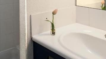 A bathroom with a white sink, a mirror, and a single rose in a vase.