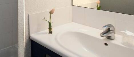 Un baño con un lavamanos blanco, un espejo y una sola rosa en un jarrón.