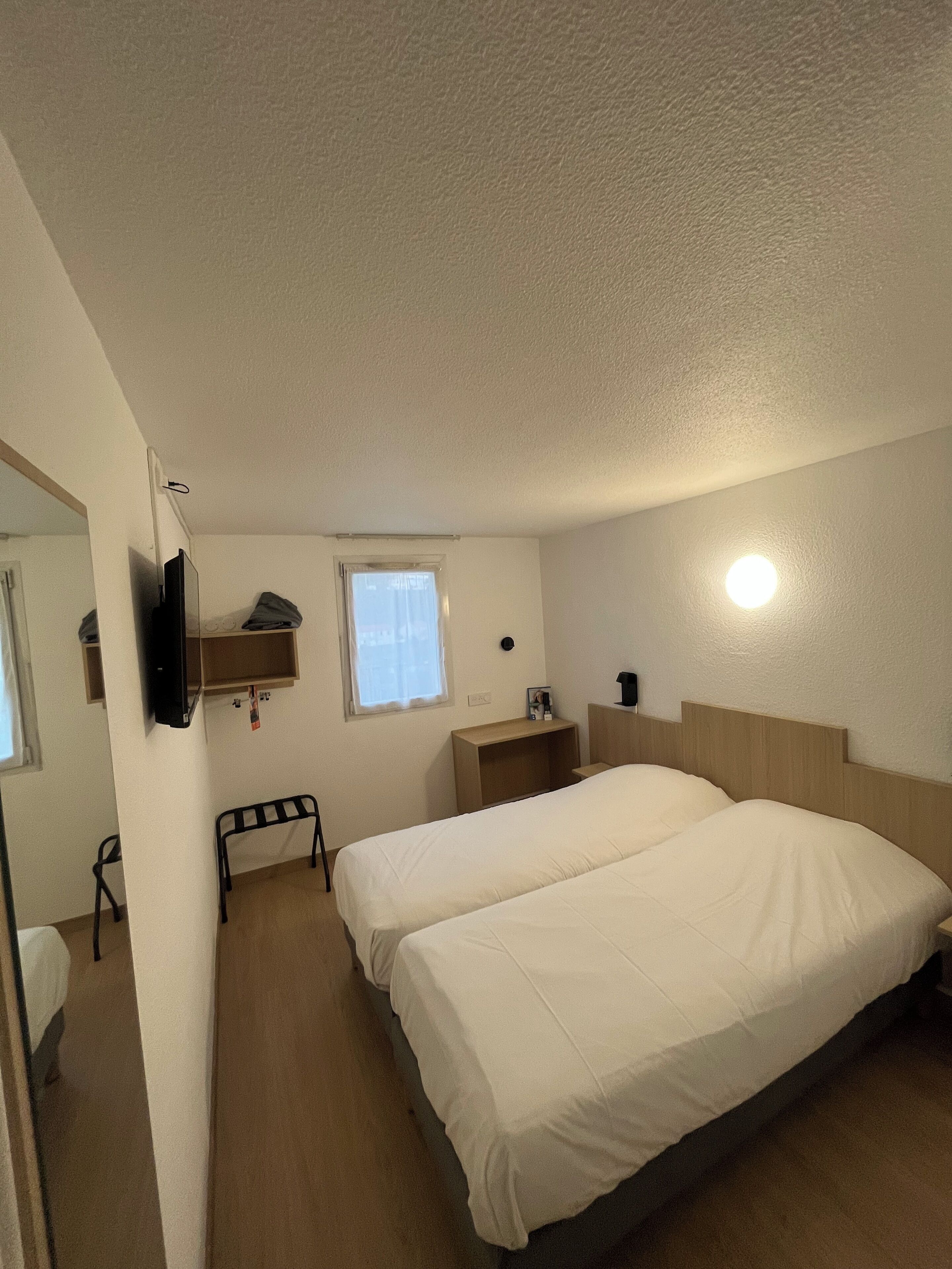 A hotel room with two beds, a desk, a chair, a TV, and a window.