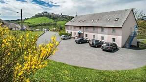 A building with a sloped roof, a staircase, and a parking area with cars. - Brit Hotel Essentiel St Flour (Saint-Flour)