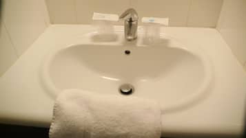Un lavabo blanc dans une salle de bain, avec un robinet argenté, un drain et une serviette blanche suspendue sur le côté.