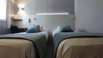 A hotel room with two beds, a desk, a chair, and a wall-mounted phone.