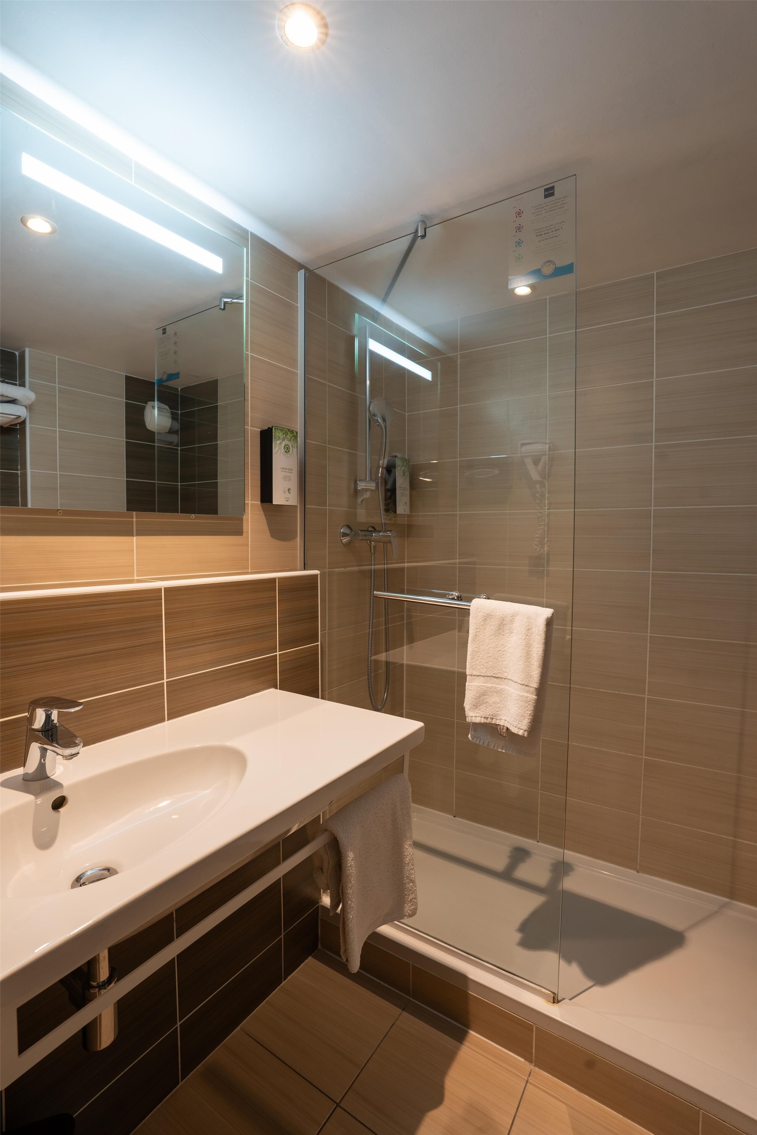 A modern bathroom with a large mirror, a sink, a shower, and a towel rack.