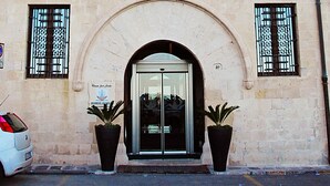 Un edificio con una amplia entrada en arco, dos ventanas con cortinas azules y dos macetas con plantas en la entrada.