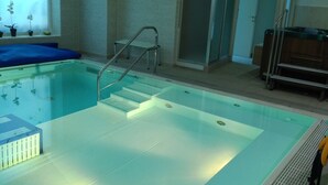 Una piscina con agua cristalina, un suelo azul y un cerramiento de vidrio.