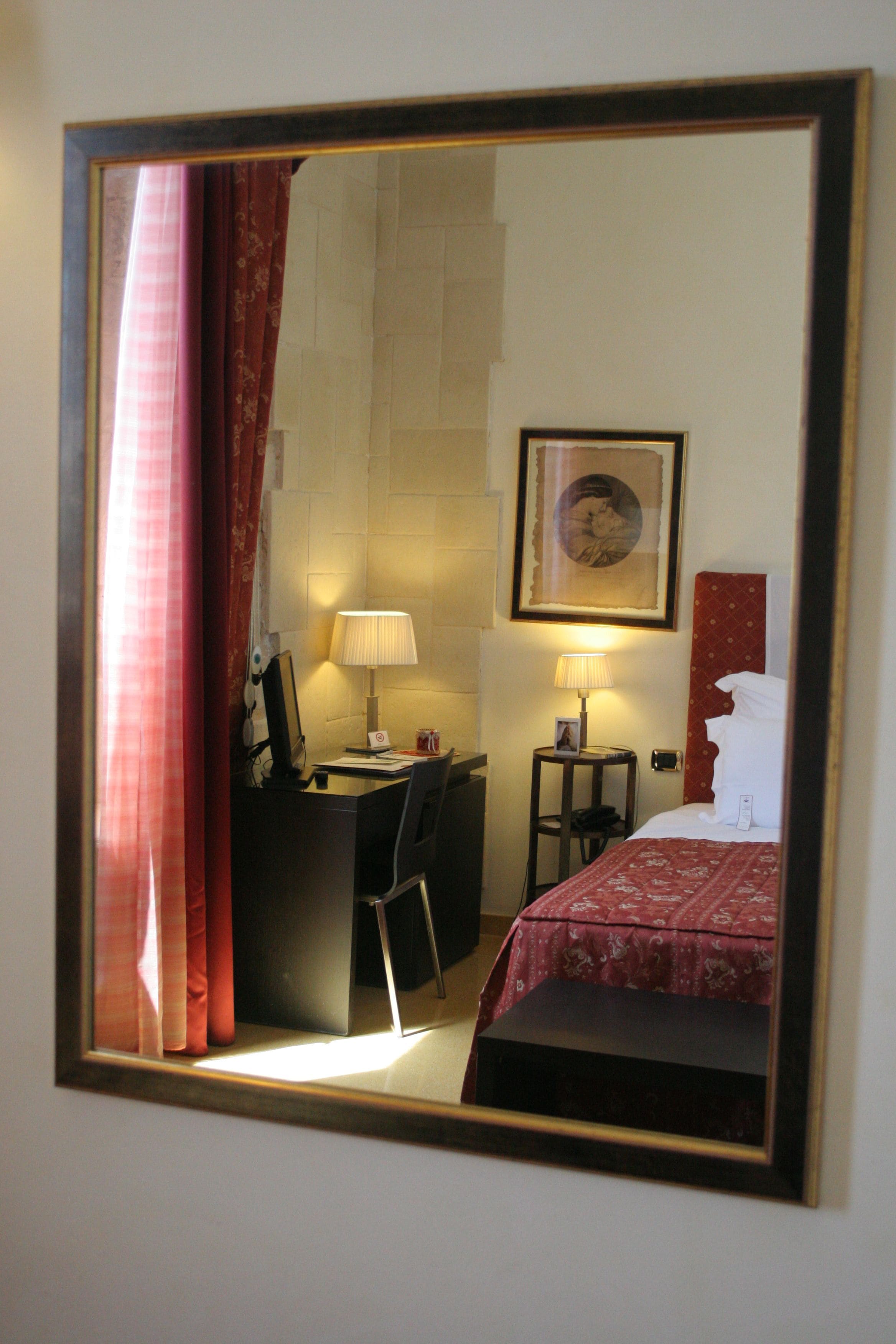 A hotel room with a bed, desk, chair, lamp, and a framed picture on the wall.