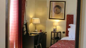 A hotel room with a bed, desk, chair, lamp, and a framed picture on the wall.