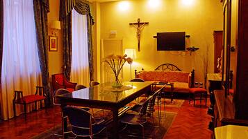 A hotel room with a dining table, chairs, a sofa, a TV, and a crucifix on the wall.