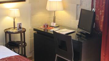 A hotel room with a bed, a desk with a computer, two lamps, and a framed picture on the wall.