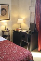 A hotel room with a bed, a desk with a computer, two lamps, and a framed picture on the wall.