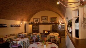 A restaurant with multiple tables, each covered with a tablecloth and set with cutlery and glasses. There are wine bottles displayed on shelves above the tables. - Podere Violino (Sansepolcro)