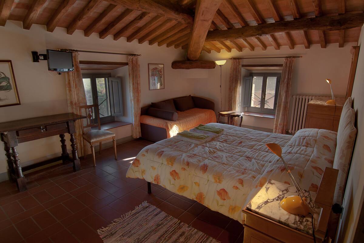 A bedroom with a bed, a desk, a chair, a lamp, and a window.