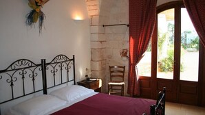 A bedroom with a bed, a chair, a nightstand, a wall-mounted light, and a window with curtains. - Masseria Morrone (Ostuni)